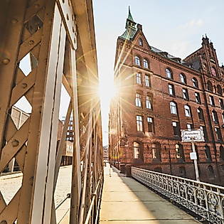 Sonnenlicht fällt durch eine Stahlbrücke auf ein historisches Speichergebäude am Sandtorkai in Hamburg