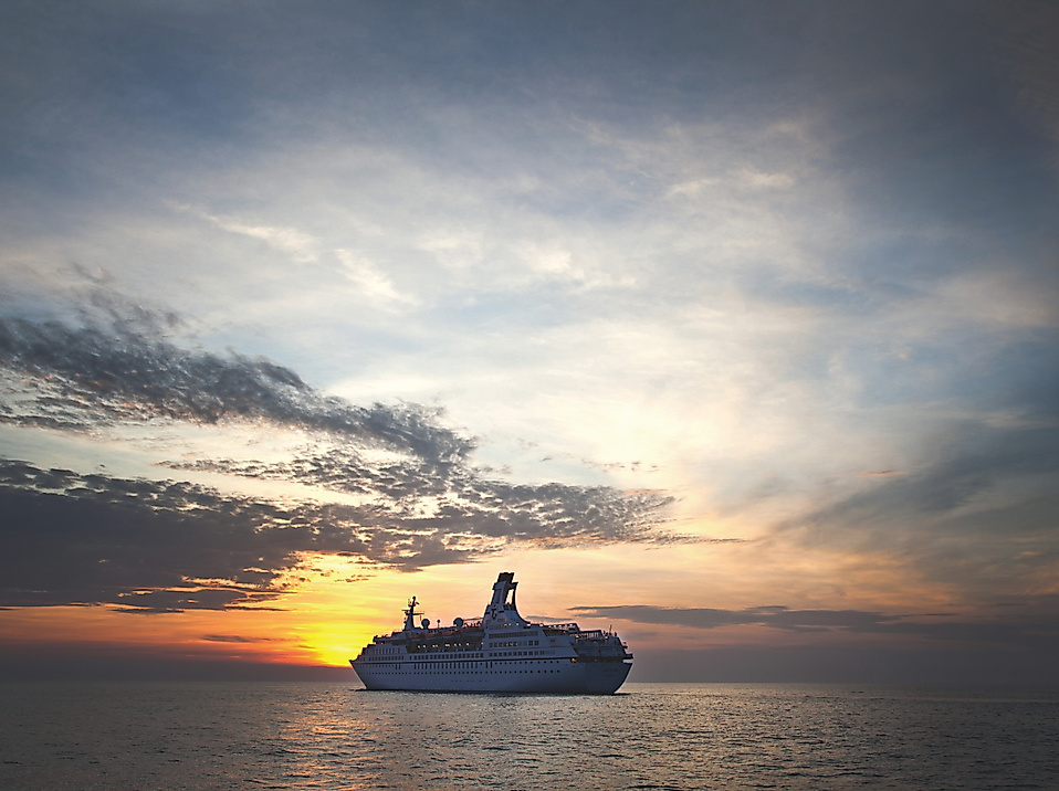 Kreuzfahrtschiff Astor bei Sonnenuntergang auf ruhiger See unter teils bewölktem Himmel