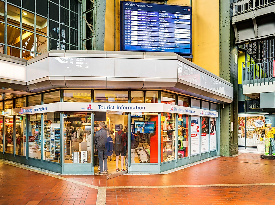 Eingang der Tourist-Information im Hauptbahnhof Hamburg mit großem Infoschild und digitaler Anzeigetafel.