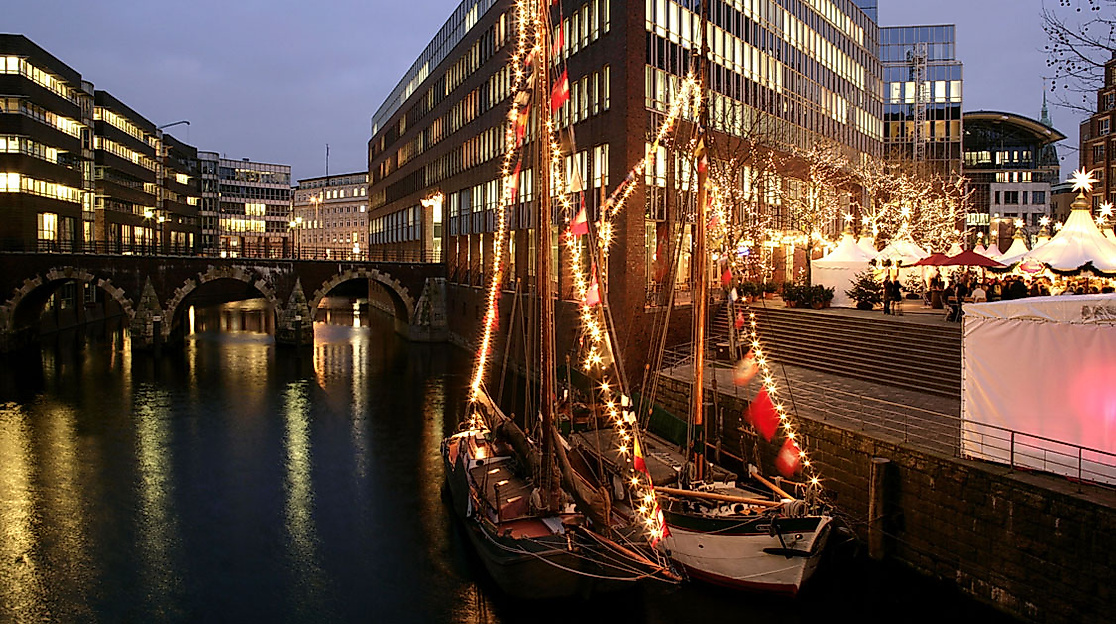 Festlich beleuchtetes Segelschiff am Nikolaifleet in Hamburg vor weihnachtlich geschmückten Gebäuden am Abend