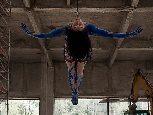 A person is hanging upside down in an industrial building with their arms outstretched.