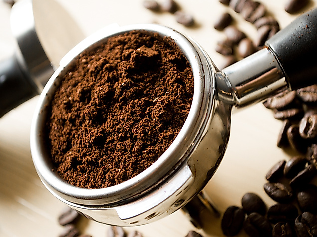 Frisch gemahlener Kaffee im Siebträger, umgeben von gerösteten Bohnen auf hellem Untergrund