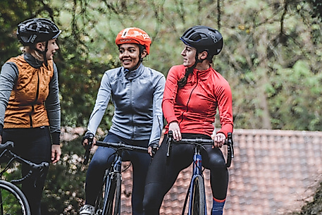 Drei Radfahrer:innen mit Helmen machen Pause im Grünen und unterhalten sich auf einem Waldweg