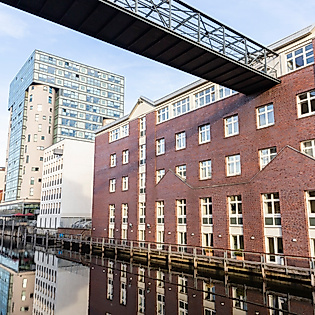 Silo 16 mit gläserner Fassade am Harburger Kanal zwischen historischen Backsteinbauten und Fußgängerbrücke