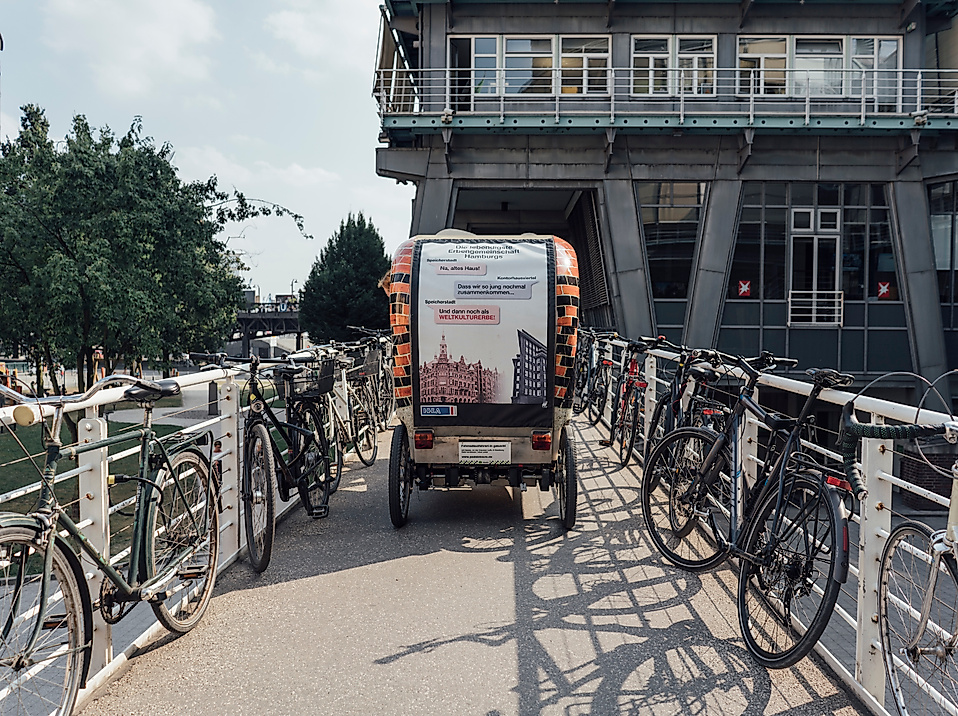 Rikscha auf Brücke zwischen abgestellten Fahrrädern vor modernem Gebäude in Hamburg