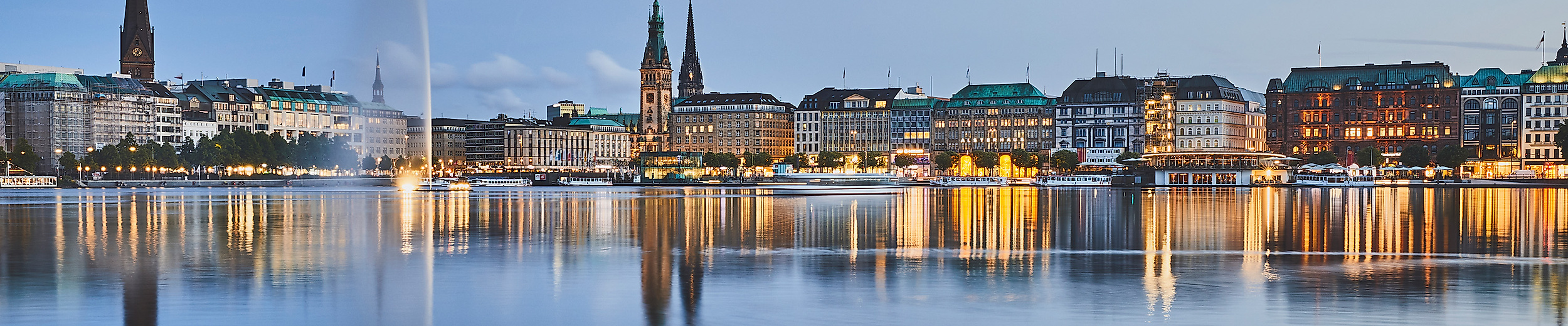 Binnenalster bei Nacht mit beleuchteter Stadtsilhouette, Alsterfontäne und Spiegelung im Wasser