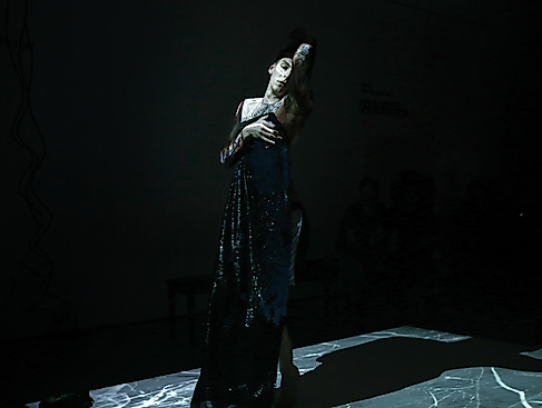 A person in a dark, shimmering dress on stage.