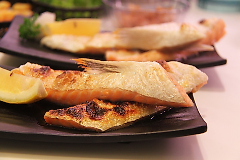 Gegrillte Fischfilets mit Zitronenscheiben auf dunklen Tellern appetitlich angerichtet