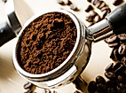 Frisch gemahlener Kaffee im Siebträger, umgeben von gerösteten Bohnen auf hellem Untergrund