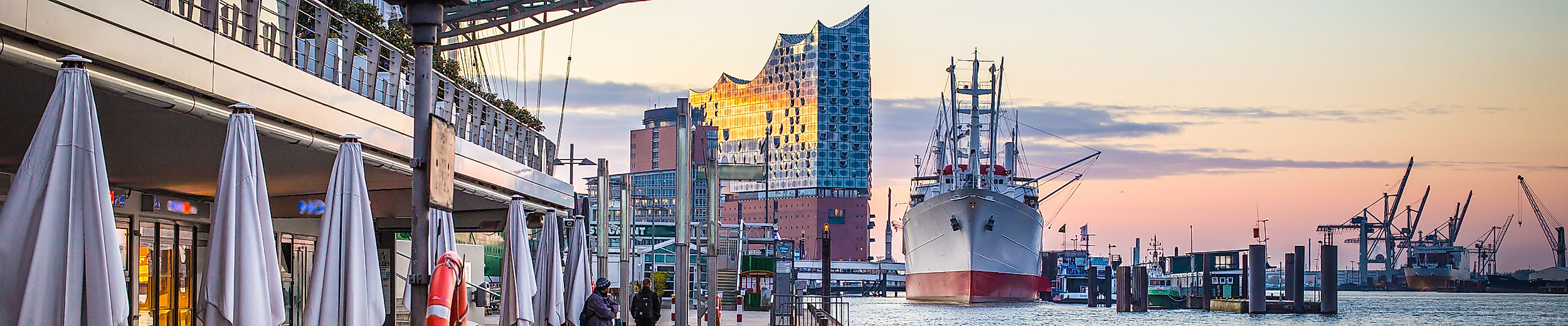 Blick von den Landungsbrücken auf die Elbphilharmonie bei Sonnenuntergang mit Schiffen und Promenade
