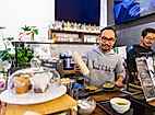 Zwei Köche bereiten asiatische Speisen an einer modernen Theke zu, im Vordergrund Kuchen unter Glasglocke