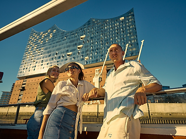 Three people on a boat in front of the Elbphilharmonie concert hall.