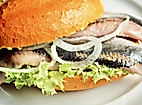 Fischbrötchen mit Matjes, Zwiebelringen und Salat auf einem weißen Teller serviert