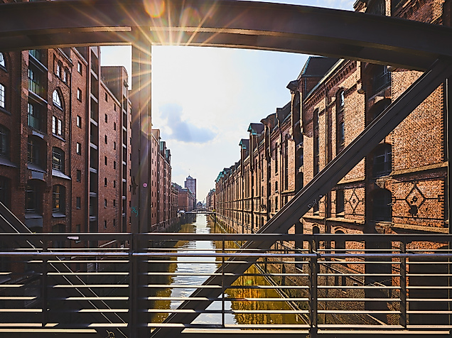Blick durch eine Stahlbrücke auf die sonnenbeschienenen Backsteinfassaden der Speicherstadt entlang des Fleets