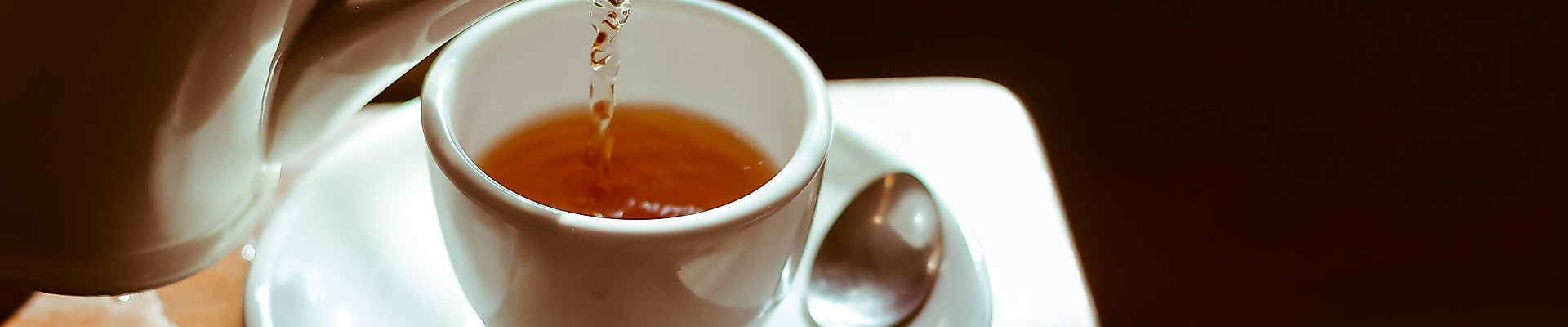 Tee wird in weiße Porzellantasse gegossen, warmes Licht sorgt für gemütliche Atmosphäre bei Tea Tim