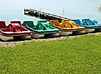 Bunte Tretboote am Ufer nebeneinander aufgereiht, bereit zur Ausleihe an einem sonnigen See