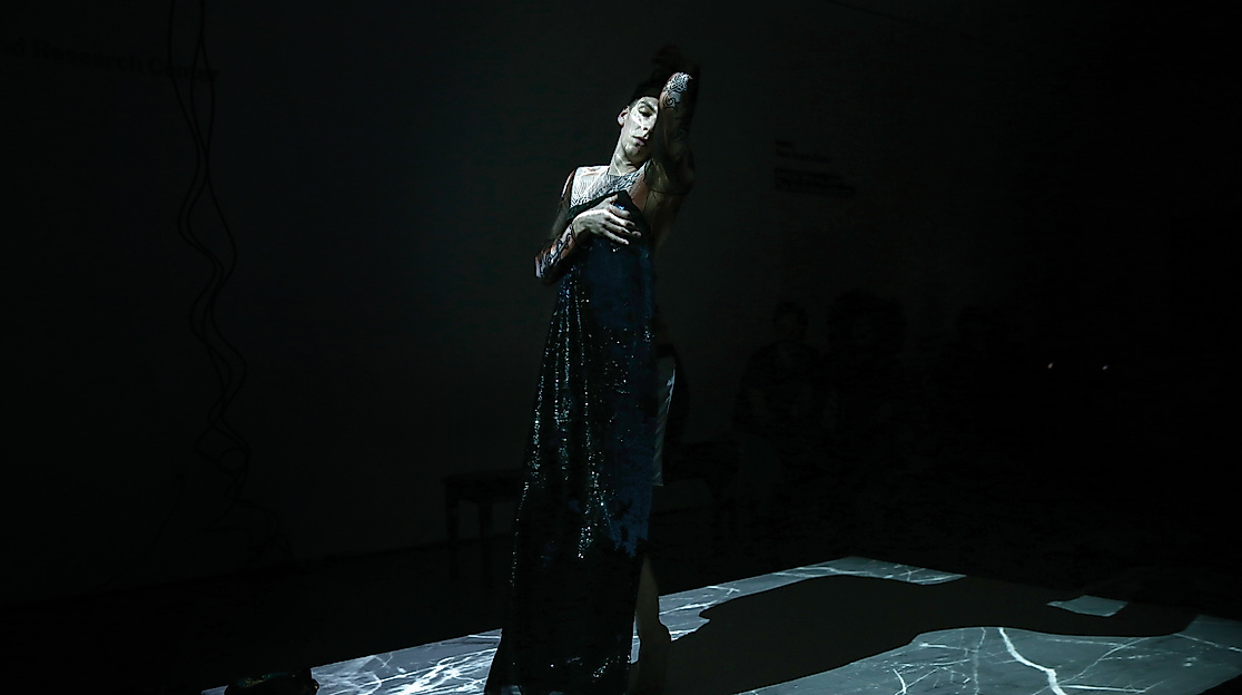 A person in a dark, shimmering dress on stage.