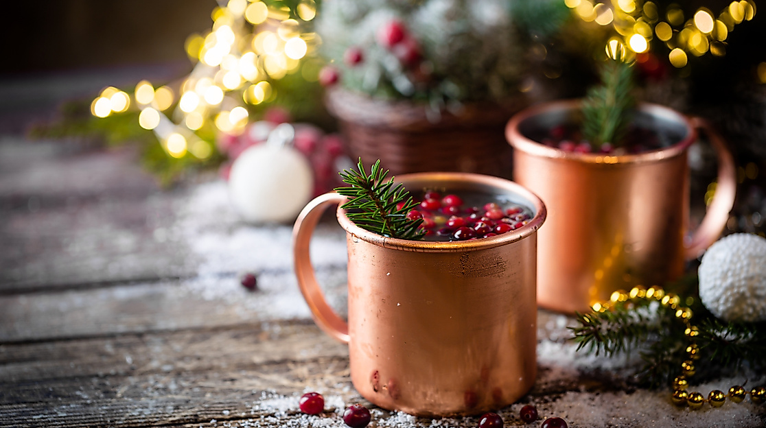 Mulled wine with cranberry in copper mug with christmas decorations on wooden table