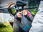 Paintball-Spieler mit Schutzmaske und Markierer zielt konzentriert hinter einer Deckung im Spielfeld