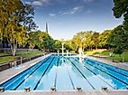 Leeres Schwimmbecken im Sommerfreibad Kaifu, umgeben von Liegewiese und Bäumen bei klarem Himmel