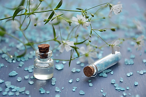 Kleine Glasfläschchen mit Badezusatz und blauen Kristallen auf dekorativer Wellness-Oberfläche