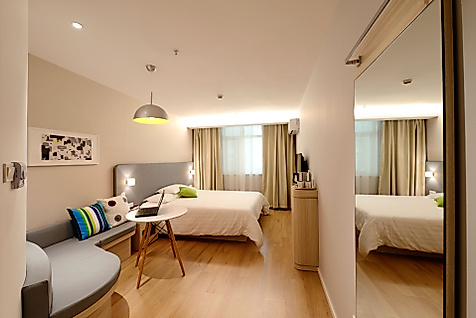 Modern eingerichtetes Hotelzimmer mit Doppelbett, Sitzecke und Schreibtisch in warmem Licht.
