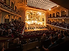 Festlich beleuchteter Opernsaal mit großem Orchester und Publikum
