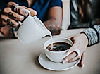 Eine Hand gießt Milch in eine Tasse Kaffee, die von einer anderen Person gehalten wird