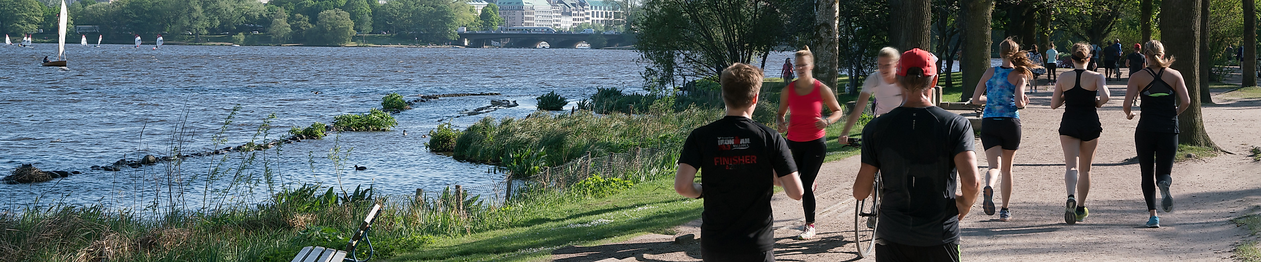 Jogger und Spaziergänger auf dem Alsteruferweg bei sommerlichem Wetter in Hamburg