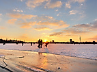 Menschen laufen Schlittschuh auf zugefrorener Alster bei Sonnenuntergang mit Blick auf Hamburgs Skyline
