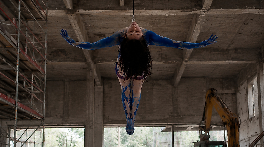 A person is hanging upside down in an industrial building with their arms outstretched.