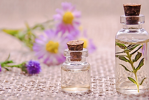 Zwei Fläschchen mit ätherischem Öl neben lila Blüten auf Leinenuntergrund